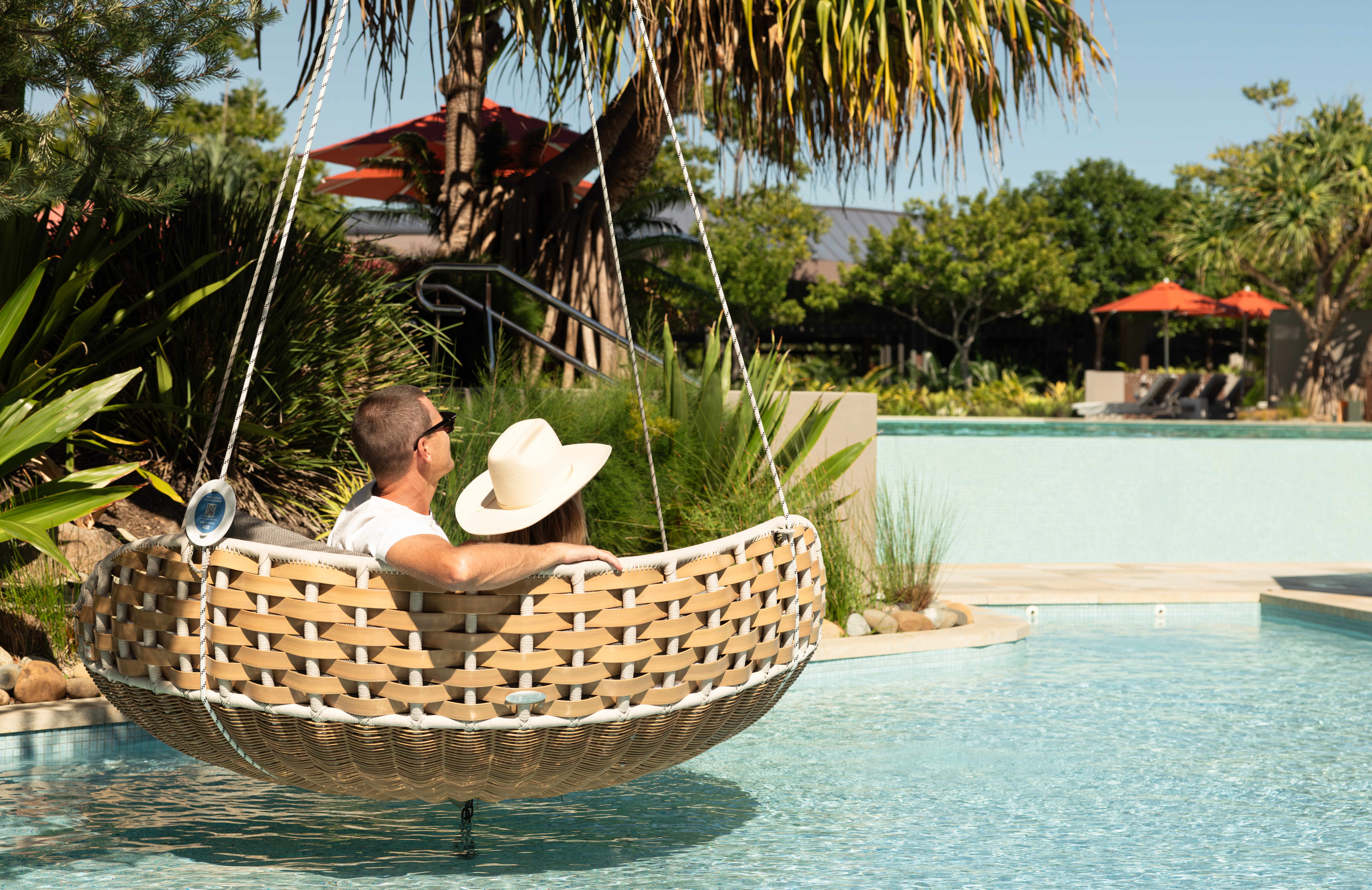 Hotel guests sitting in wicker chair floating above the pool - Elements of Byron