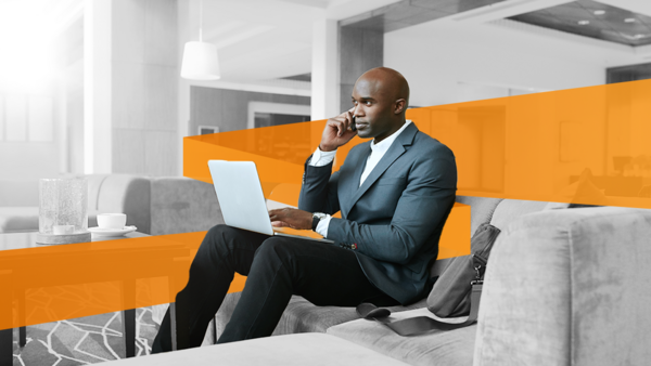 A businessman working on his laptop and phone, sitting in the common area of a hotel