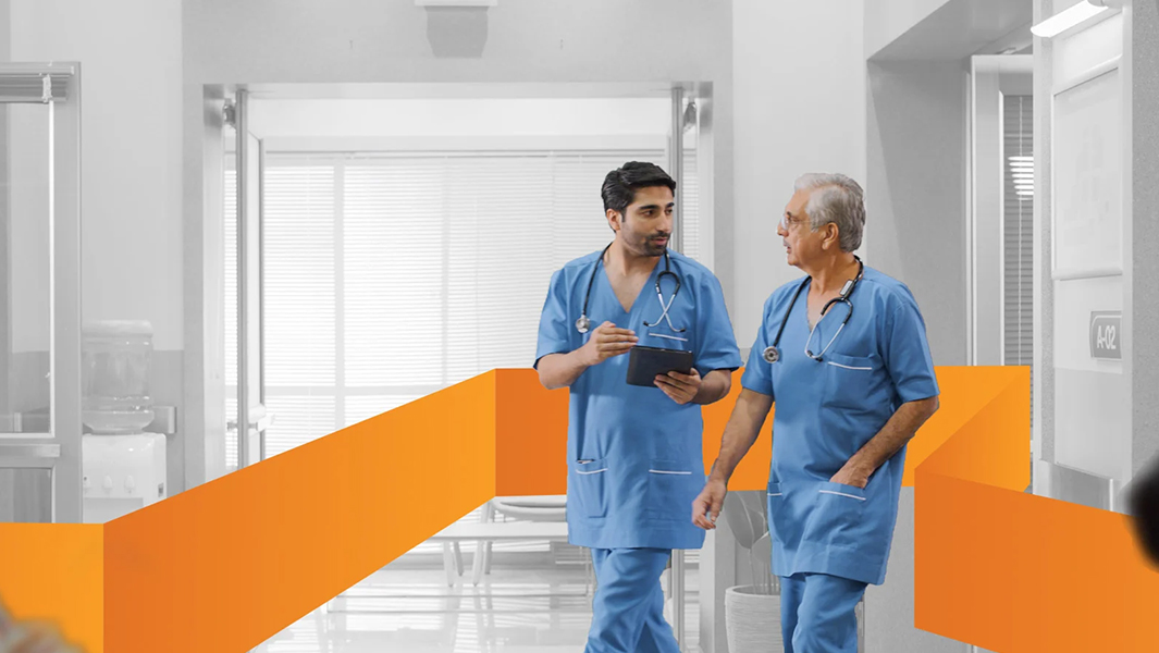 Two doctors in scrubs talking and reviewing notes on a tablet as they walk down a hallway